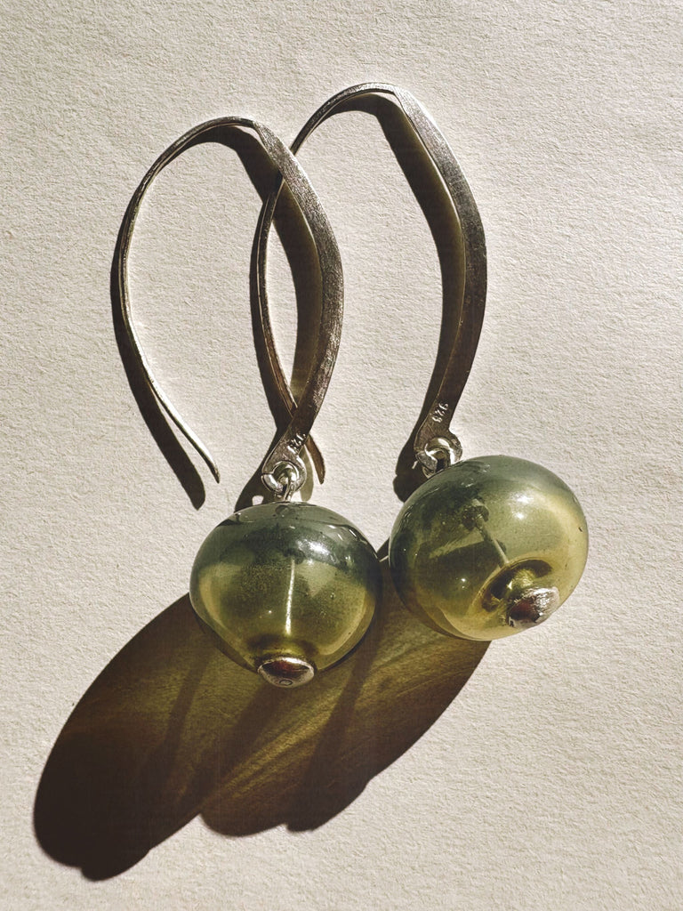 Pair of green glass bead earrings with silver hoops on a light background
