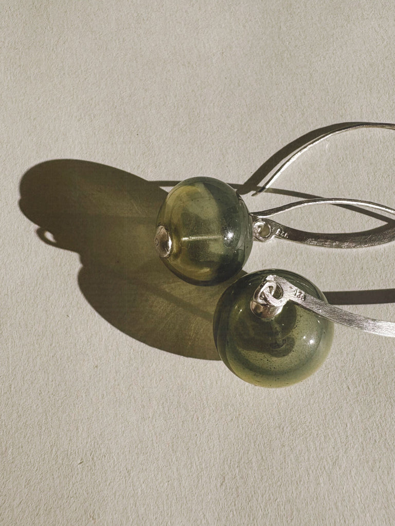Green glass earrings with silver hooks on a light gray background