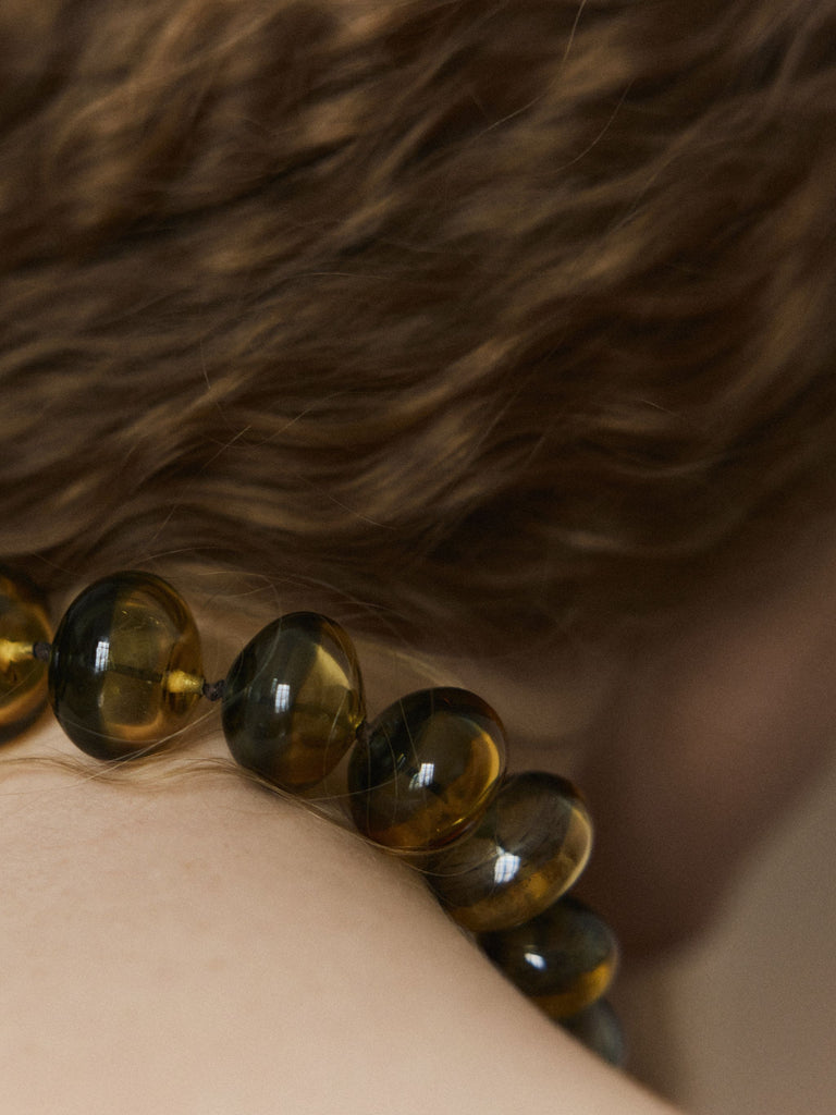 Close-up of a person wearing a yellow green Murano glass beaded necklace against long hair background