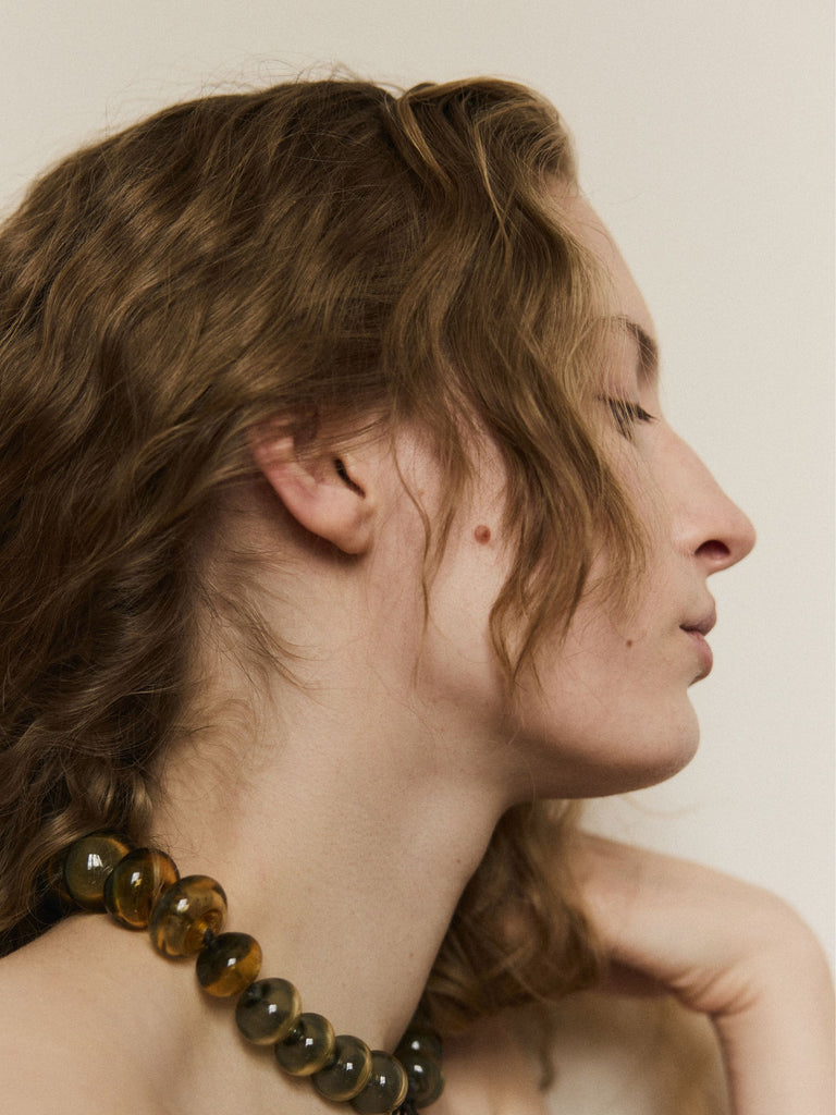 Close-up of a woman's neck and shoulder with a Murano glass beaded necklace against a neutral background