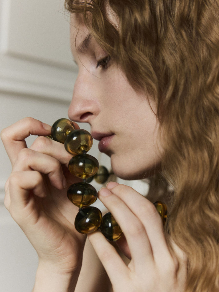 Woman holding a set of amber-colored Murano glass beads close to her face