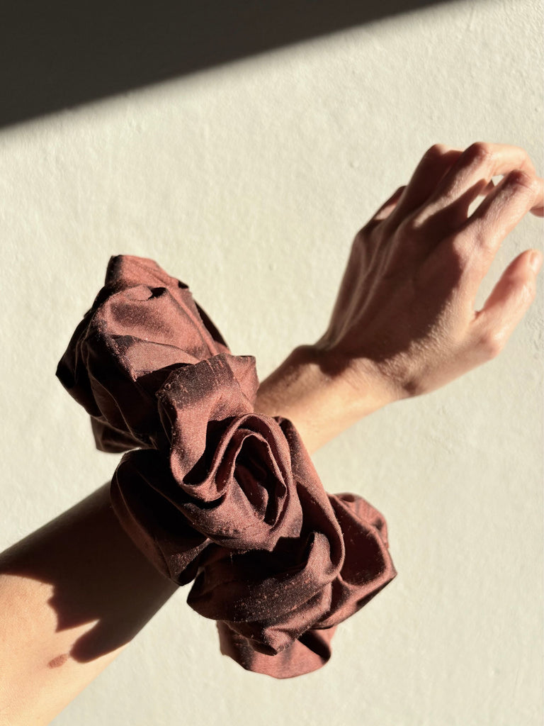 Brown silk scrunchie on a wrist with a neutral background