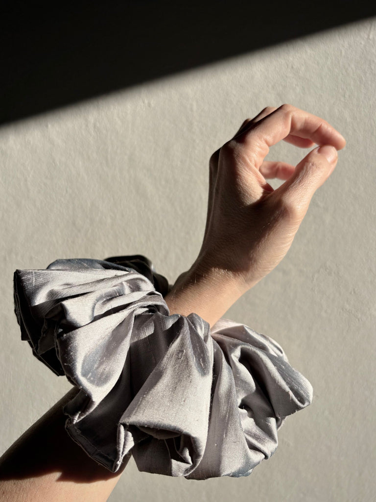 Hand wearing a silver scrunchie on a neutral background