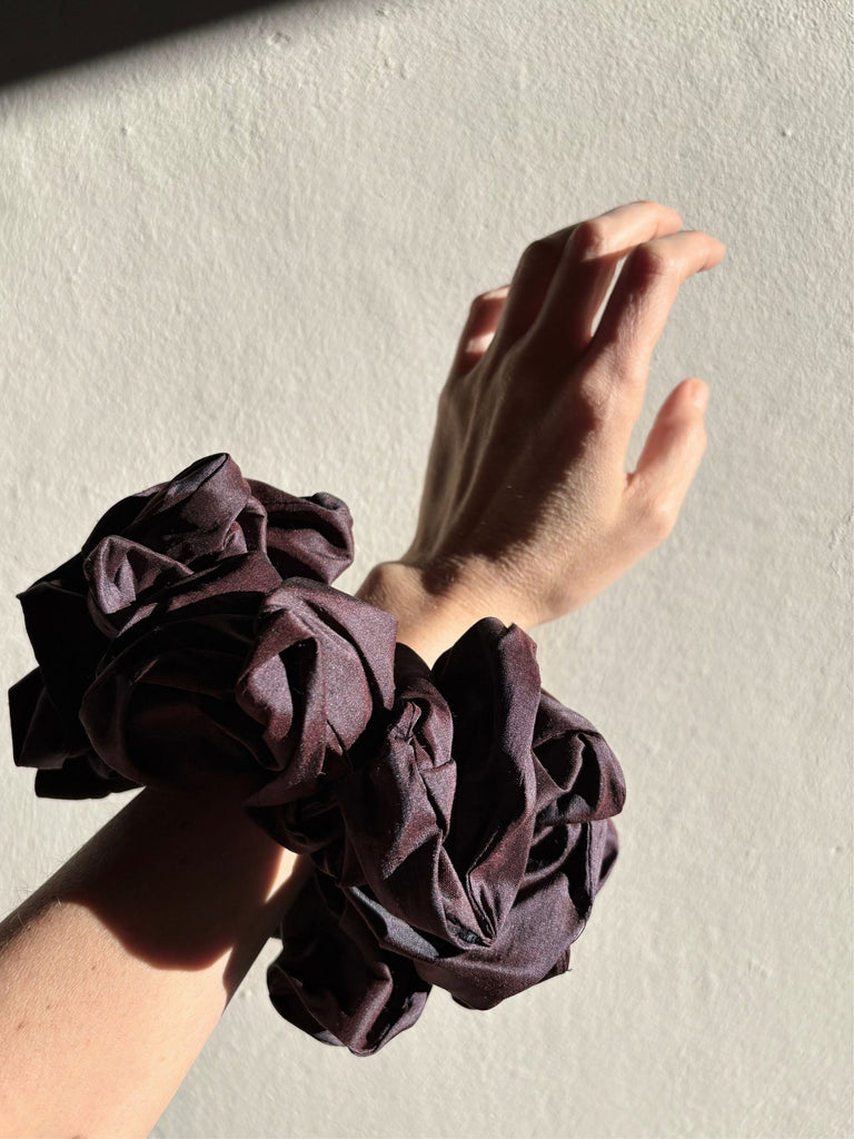Hand wearing purple silk scrunchie on a plain background