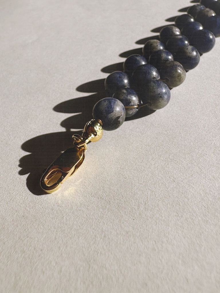 Necklace with blue Sodalite beads and a gold clasp on a light grey background