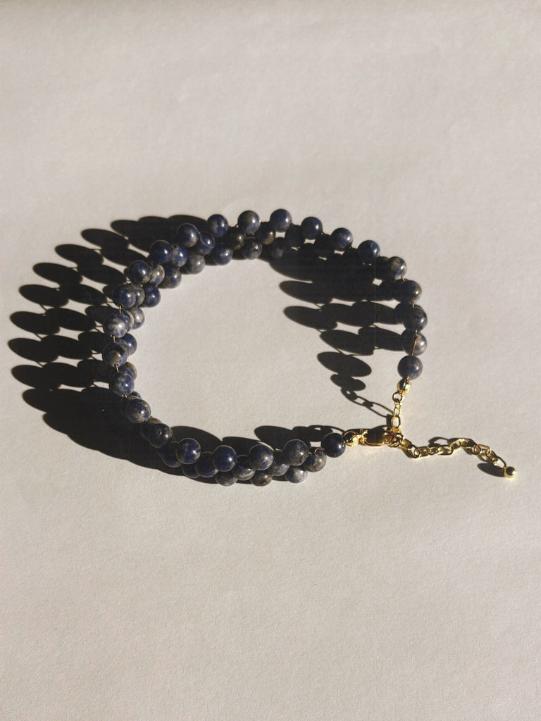 Beaded necklace with sodalite blue beads and a gold clasp on a light gray background