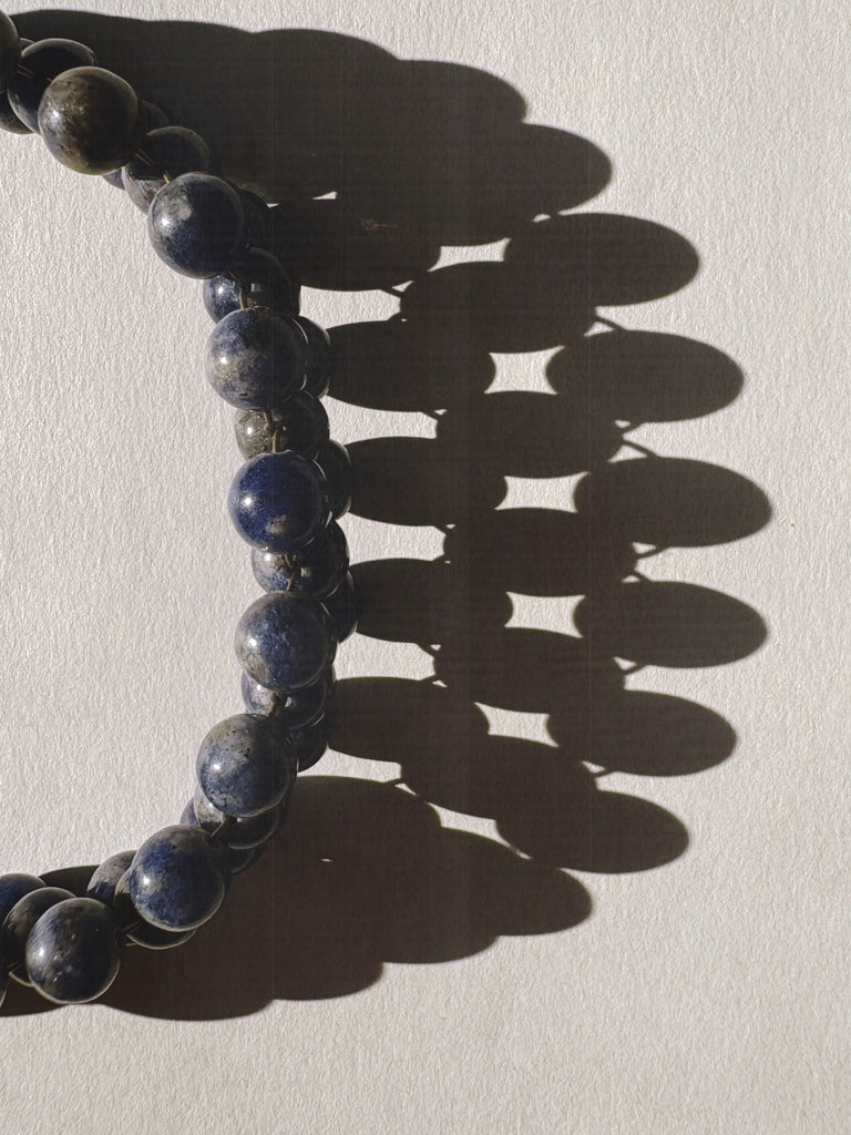 Close-up of a blue Sodalite beaded necklace casting a shadow on a light background