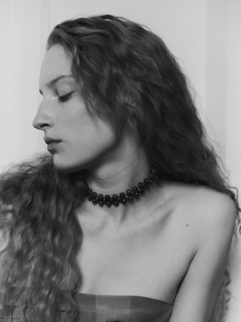 Black and white portrait of a woman with long hair and a choker beaded necklace.