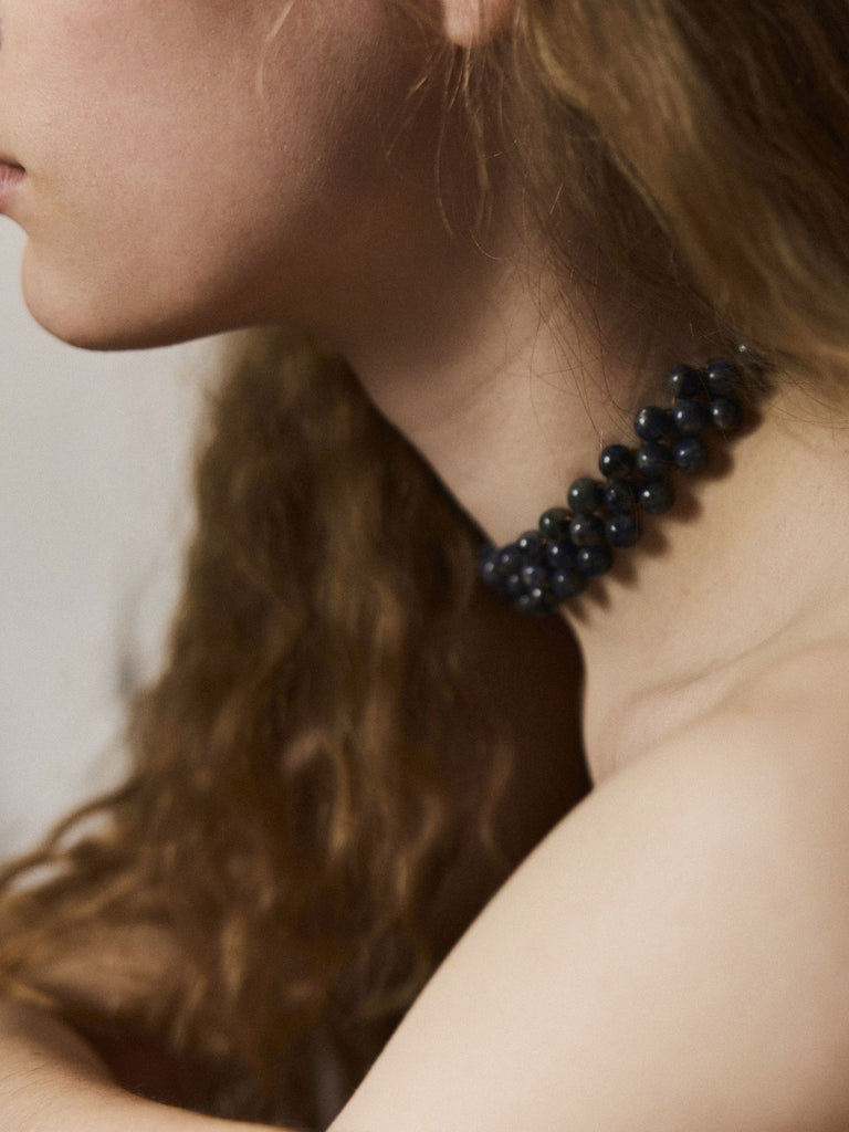 Close-up of a person wearing a blue Sodalite choker beaded necklace with a neutral background